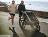 A couple running by the sea with a child trailer. Produktbild-Vorschau