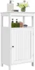 A white bathroom cabinet with a single door and an open shelf above. It is decorated with a soap dispenser, a sponge, and a small vase of flowers. Produktbild-Vorschau
