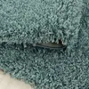 A close-up view of a teal shag rug, showing the texture of the fibers and the underside of a folded section. Produktbild-Vorschau
