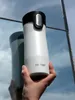 A hand holds a white Contigo travel mug in front of a reflective surface showing a sky. Anteprima dell’immagine prodotto