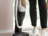 A person is holding a vacuum cleaner in a room. Voir les images du produit