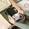 Hands packing a travel kettle into a suitcase with clothes and a perfume bottle. Produktbild-Vorschau