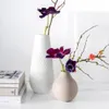 Two vases with flowers on a white surface, with books stacked to the left. Produktbild-Vorschau