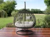 A hanging egg chair with cushions on a wooden deck in a garden setting. Náhled obrázku produktu