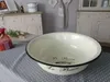 A vintage-style enamel wash bowl with text 'Le Bain' is placed on a table with a polka dot tablecloth. In the background, there are antique-style cabinets and decorative items. Produktbild-Vorschau