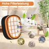Close-up of a vacuum cleaner filter with various particles illustrated around it. The background shows a living room scene with a plant and sofa. Náhľad obrázku produktu