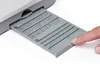 A finger is pointing to a gray insert card with symbols and letters, which is partially inserted into a sewing machine. Produktbild-Vorschau