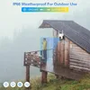 A security camera is mounted on a wooden cabin during a rainstorm, with a person standing on the porch. The image highlights the camera's weatherproof capabilities. Produktbild-Vorschau