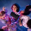 A group of young people are gathered around a Bluetooth speaker, enjoying music. Produktbild-Vorschau
