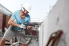 A construction worker is using a hammer drill to drill into a concrete wall. Voir les images du produit