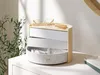 A jewelry organizer sits on a white surface next to a plant. Náhled obrázku produktu