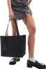 A person is holding a black tote bag and wearing black loafers and white socks. Podgląd zdjęcia produktu
