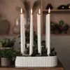 A white ribbed candle holder with five white candles and greenery on a wooden table. Produktbild-Vorschau