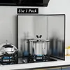 A kitchen splash guard is set up behind two pots on a stovetop. Produktbild-Vorschau