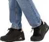 A person wearing blue jeans and black Skechers sneakers. Náhled obrázku produktu