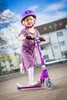 A young girl riding a purple scooter outdoors. Produktbild-Vorschau