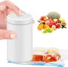 A hand presses a button on a white vacuum sealer device, with a pile of fresh fruit and vacuum-sealed bags of food in the background. Produktbild-Vorschau