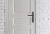 A close-up view of a white door with a dark gray door handle, set against a white brick wall. Produktbild-Vorschau