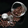 Coffee beans spilling out of a glass cup next to reusable coffee capsules. Náhled obrázku produktu