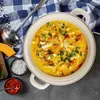 A pot of soup is shown with ingredients and serving utensils. Produktbild-Vorschau