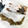 A box of teabags and loose tea leaves are arranged on a white wooden surface, with a teapot in the background. Produktbild-Vorschau
