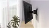 A TV wall mount is attached to a wall, with a TV attached to it. A plant is in the foreground. Anteprima dell’immagine prodotto