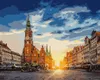 A painting of a town square with a clock tower and buildings, illuminated by the setting sun. Podgląd zdjęcia produktu