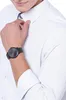 A close-up shot of a person wearing a black watch on their left wrist, with their hand resting on their chest, against a white background. Anteprima dell’immagine prodotto