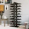 A modern living room or bar area with a black metal wine rack filled with wine bottles, a table with a lamp and decorative items, and a concrete wall. Podgląd zdjęcia produktu