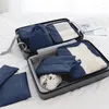 An open suitcase filled with various blue packing cubes and a pair of white sneakers, laid out on a white bed. Anteprima dell’immagine prodotto