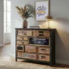 A vintage-style apothecary cabinet with multiple drawers, decorated with various vintage-themed prints and labels. It is placed in a room with a framed picture and a lamp on top, suggesting a home decor setting. Podgląd zdjęcia produktu