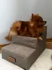A small brown dog is lying on a beige, three-step pet ramp. Náhled obrázku produktu