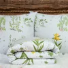 A folded duvet and two pillows with a botanical print are arranged on a white fluffy surface in front of a wooden headboard. Produktbild-Vorschau