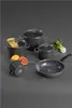 A set of dark gray cookware, including pots, a frying pan, and a small pitcher, arranged on a gray surface with some food items like spaghetti, oranges, and bok choy. Anteprima dell’immagine prodotto