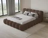 A bedroom scene with a large, upholstered bed as the focal point, set against large windows with a view of greenery. Voir les images du produit