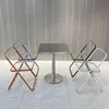 A small square table with four chairs around it, set in a modern room with a textured wall and tiled floor. Anteprima dell’immagine prodotto