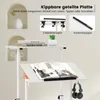 A close-up view of a white mobile standing desk with a book open on the tilted surface and headphones hanging from a hook. Podgląd zdjęcia produktu