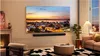 A modern living room with a large TV displaying a cityscape at sunset, a soundbar mounted below it, and a pink sofa. Anteprima dell’immagine prodotto