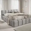 A modern, upholstered bed with a tufted headboard and base, set in a softly lit bedroom with sheer curtains. Náhled obrázku produktu