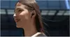 A woman wearing black wireless earbuds, with her hair blowing in the wind. Podgląd zdjęcia produktu
