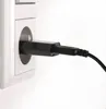 A black USB power adapter is plugged into a white electrical socket. Produktbild-Vorschau