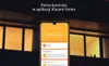 A smartphone displaying a smart home app interface is shown in front of a blurred background of a building at night. Produktbild-Vorschau