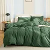 A neatly made bed with dark green bedding in a room with white curtains and blinds. Produktbild-Vorschau