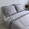 A close-up view of a bed with gray bedding, featuring ruffled edges on the pillows and duvet cover. Produktbild-Vorschau
