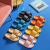 Mehrere Paare einfarbiger Slide-Sandalen in Schwarz, Blau, Orange, Gelb, Beige und Pink auf blauem Boden angeordnet Náhľad obrázku produktu