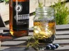A bottle of Kentucky Bourbon and a mason jar cocktail with blueberries and rosemary on a wooden table. Voir les images du produit