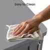 A hand is wiping a grey surface with a cloth, suggesting ease of cleaning. Voir les images du produit