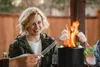A group of people are gathered around a small fire pit, roasting marshmallows. Voir les images du produit