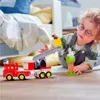 A young child plays with LEGO DUPLO fire truck toys on the floor next to a bed. Produktbild-Vorschau