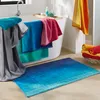 A bathroom scene with towels draped over a bathtub and a bath mat on the floor. Produktbild-Vorschau